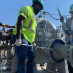 Technicians checking a pump piping flange connection for pipe strain during installation