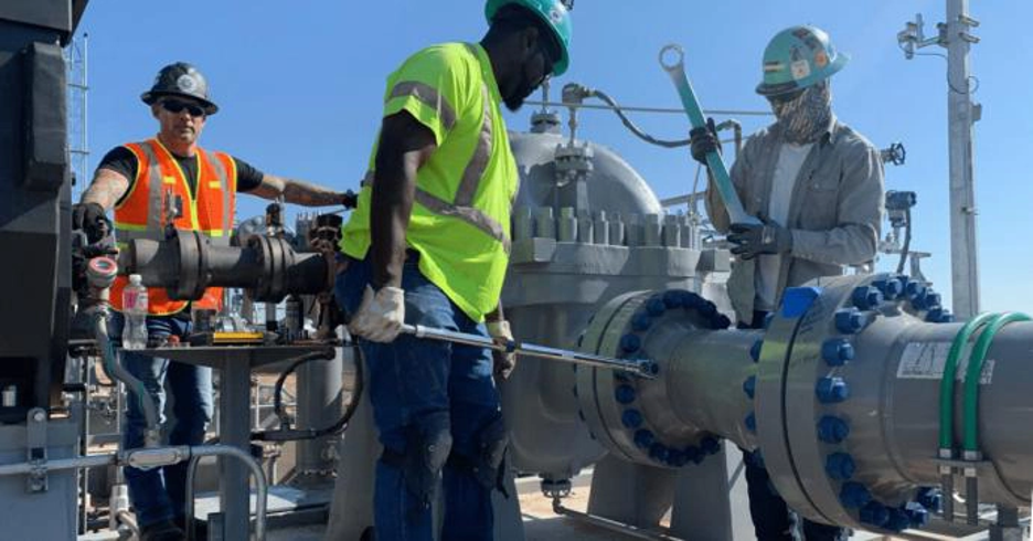 Technicians checking a pump piping flange connection for pipe strain during installation