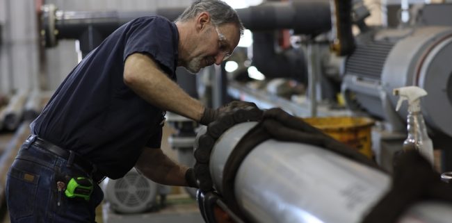 Technician fitting large pump piping during equipment installation